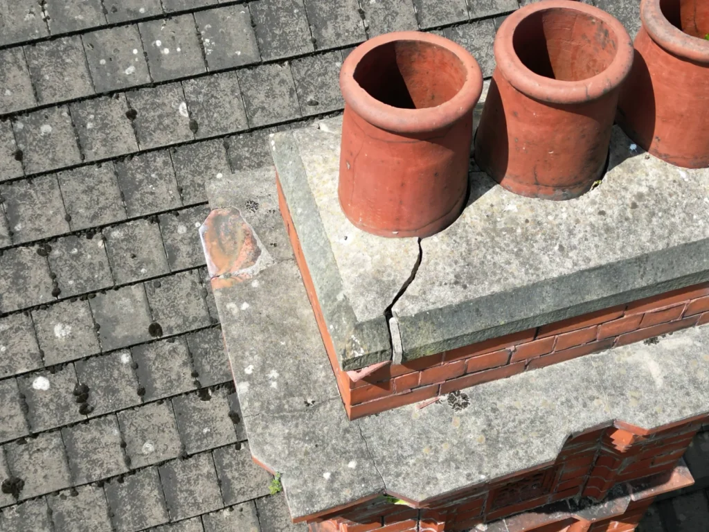 Drone close-up of a cracked concrete chimney crown and clay pots